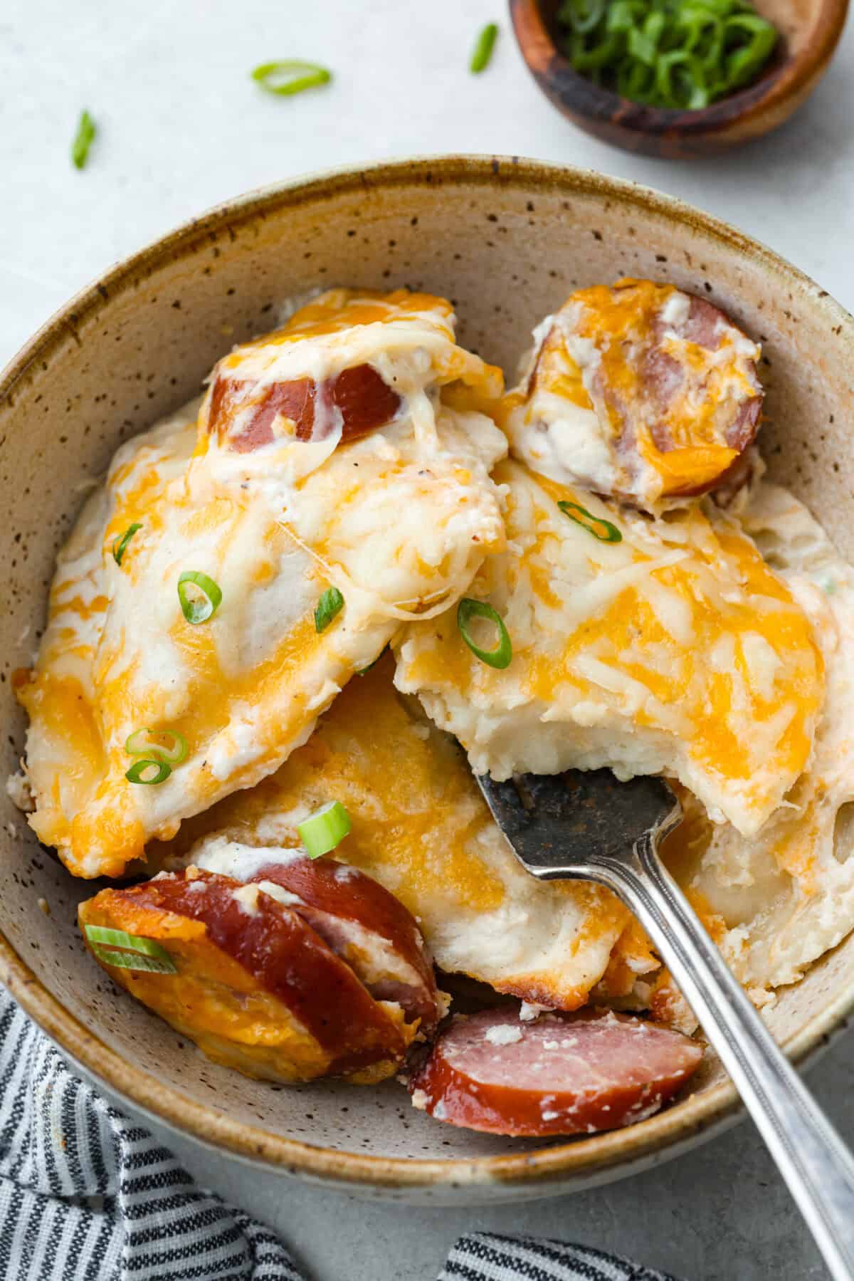 This isn’t your average Pierogi Casserole. While most stick to one type of cheese, I use a blend for ooey-gooey cheesy creaminess and cozy flavor in every bite. A bowl of pierogi casserole with kielbasa and a fork.