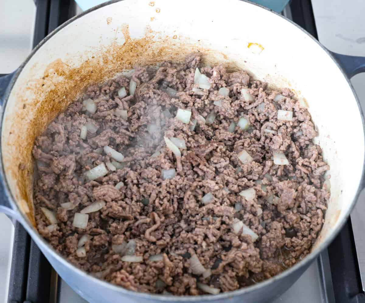 Not to be dramatic, but Frito Chili Pie might have saved my sanity. Zero whining, zero leftovers, it was a total dinner miracle. Crunchy, flavorful and ridiculously easy... you need this in your life ASAP. Ground beef and onions cooking in a pot.