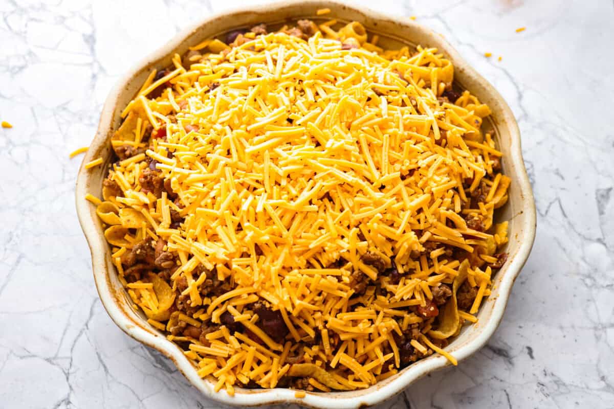 Not to be dramatic, but Frito Chili Pie might have saved my sanity. Zero whining, zero leftovers, it was a total dinner miracle. Crunchy, flavorful and ridiculously easy... you need this in your life ASAP. Cheese added to the top of the Frito Chili pie ready to go in the oven.