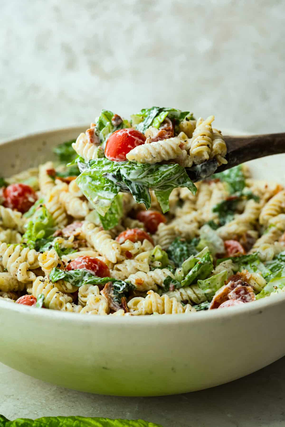 The best sandwich ever? Hands down, a BLT. Add in my obsession with pasta salads and, chef’s kiss! This BLT Pasta Salad has the crispy bacon, juicy tomatoes, and crunchy lettuce we all love! Someone lifting a scoop of BLT pasta salad out of the large pasta bowl.