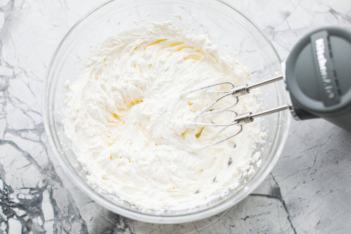 Cream cheese and sour cream being mixed together with a hand mixer. 