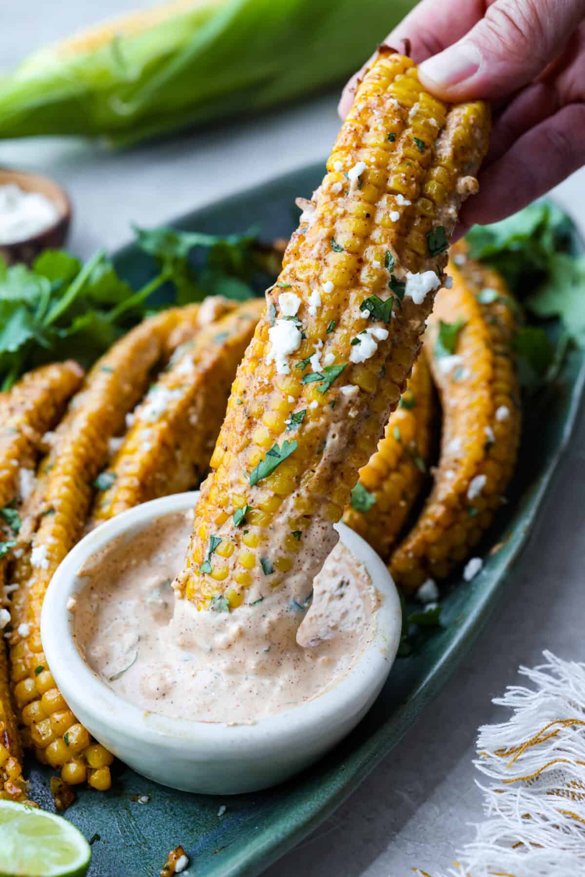 Someone dipping a corn rib into the elote sauce. 
