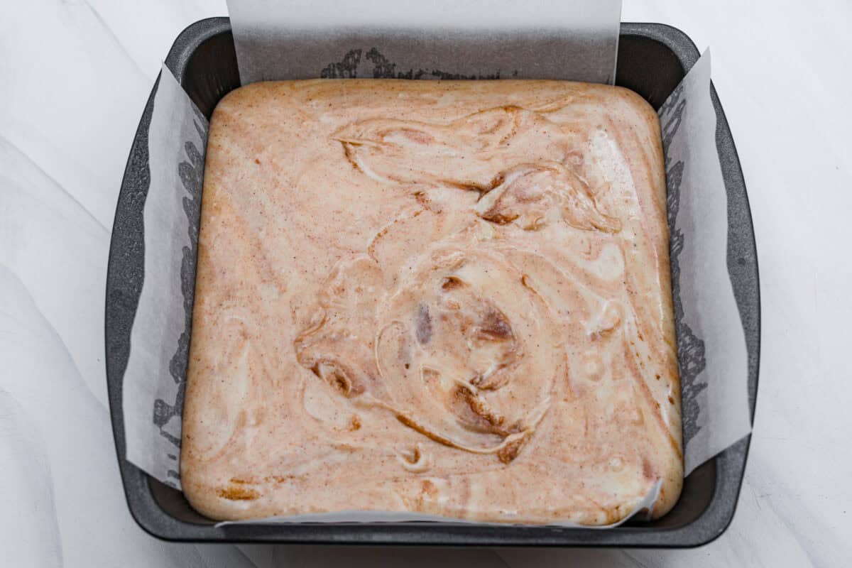 This 4-ingredient churro fudge is pure magic! It's buttery, cinnamon sugary bliss that tastes like a churro and fudge had a baby. It’s easy to make and even easier to gift (if you can resist eating it all first!). Overhead shot of the fudge mixture poured into a 8x8 pan with parchment paper.