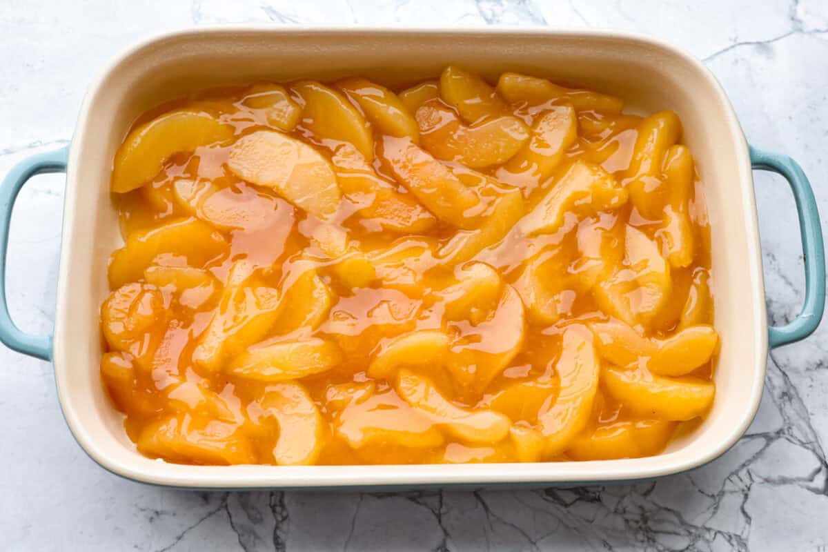 Baking dish with apple pie filling spread out on the bottom. 