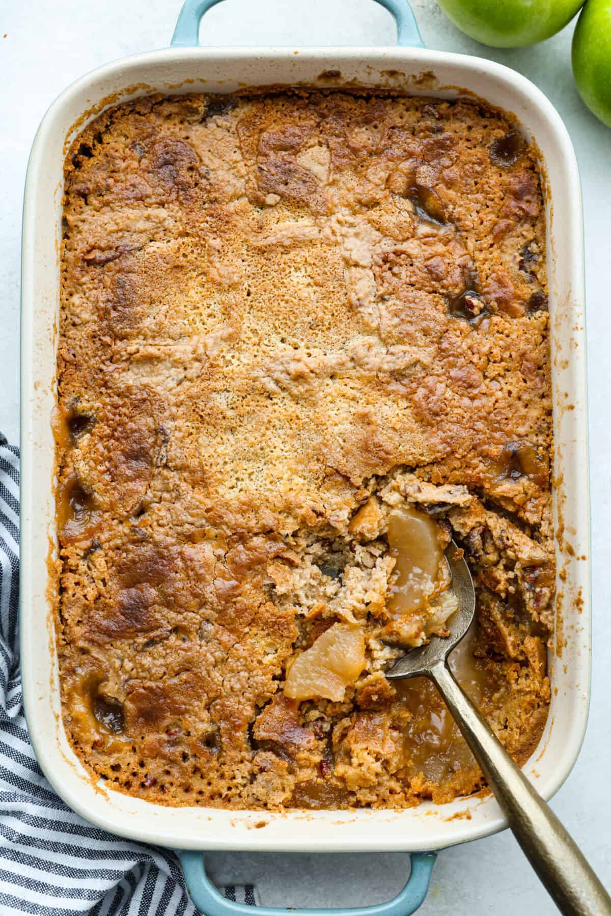 Overhead shot of apple dump cake mix in a baking dish and a serving spoon.