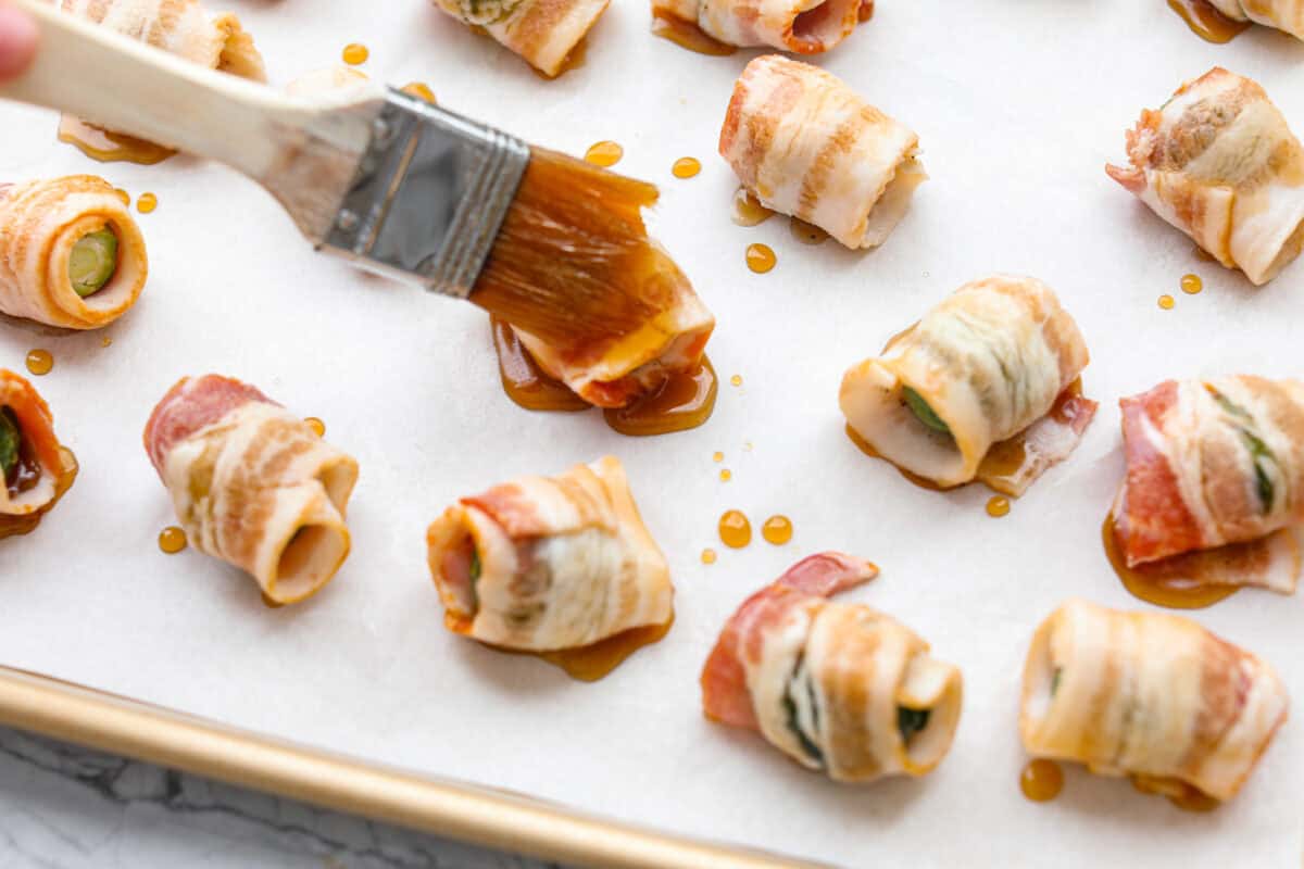 I love bacon. I love Brussels sprouts. Put them together and I’m sold. But the secret to these bacon-wrapped Brussels sprouts? A drizzle of maple syrup! It makes them sweet, smoky, and completely irresistible. Someone brushing the maple drizzle onto the bacon wrapped Brussels sprouts.
