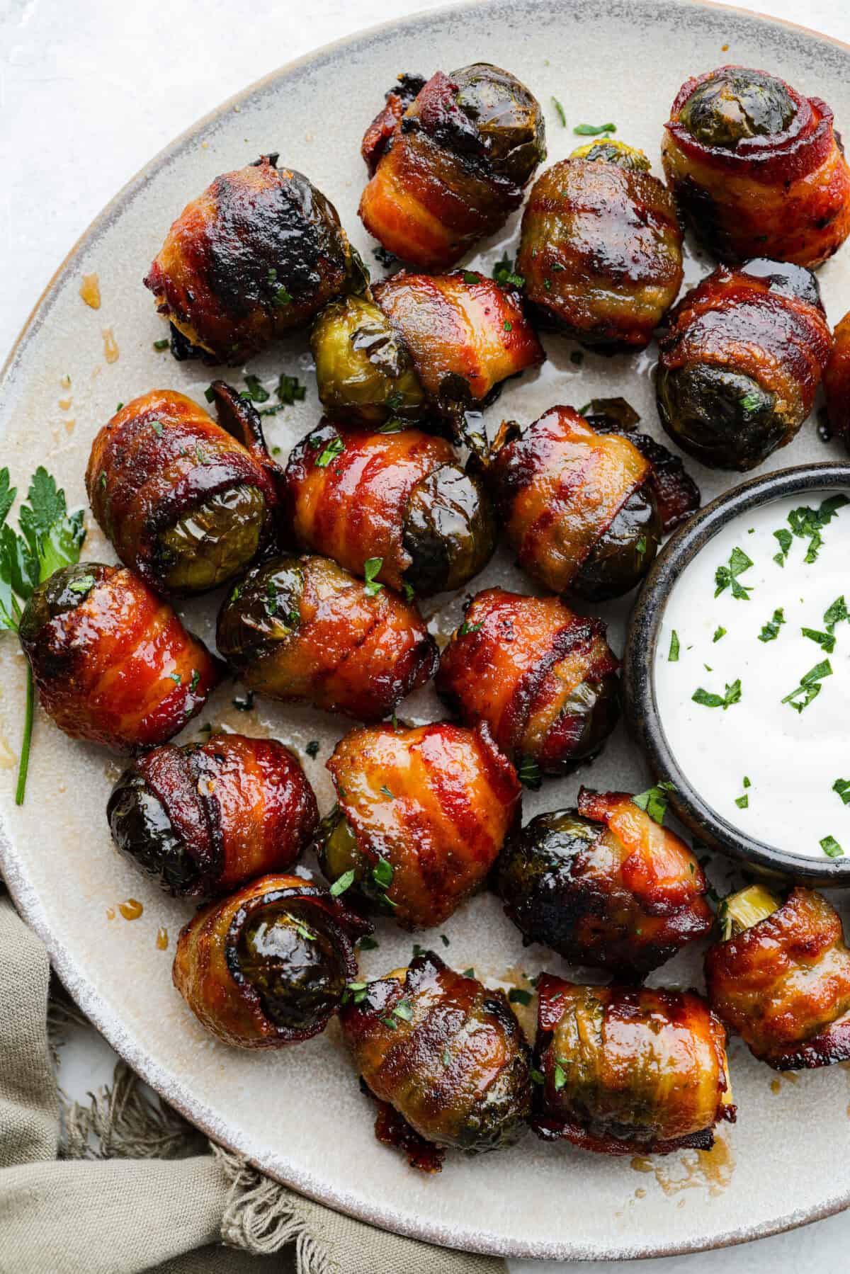 I love bacon. I love Brussels sprouts. Put them together and I’m sold. But the secret to these bacon-wrapped Brussels sprouts? A drizzle of maple syrup! It makes them sweet, smoky, and completely irresistible. A platter of bacon wrapped Brussels sprouts with some dip.