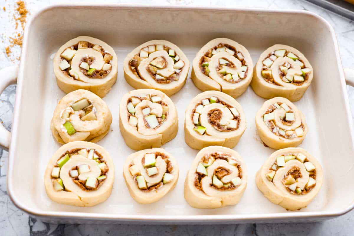 These Caramel Apple Cinnamon Rolls are soft, gooey, and baked with cozy fall flavor in every bite. The homemade dough bakes up perfectly fluffy, and the rich caramel topping makes them feel extra special. Caramel apple cinnamon rolls sliced, placed in a pan, and read to rise.