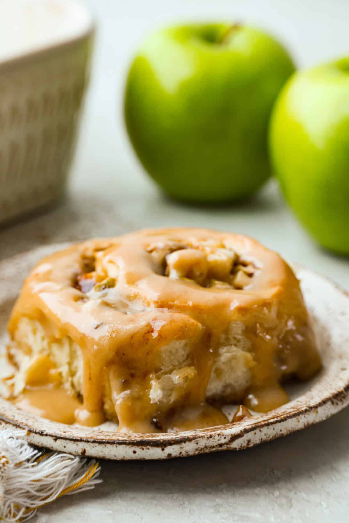 These Caramel Apple Cinnamon Rolls are soft, gooey, and baked with cozy fall flavor in every bite. The homemade dough bakes up perfectly fluffy, and the rich caramel topping makes them feel extra special. Single caramel apple cinnamon roll on a plate.