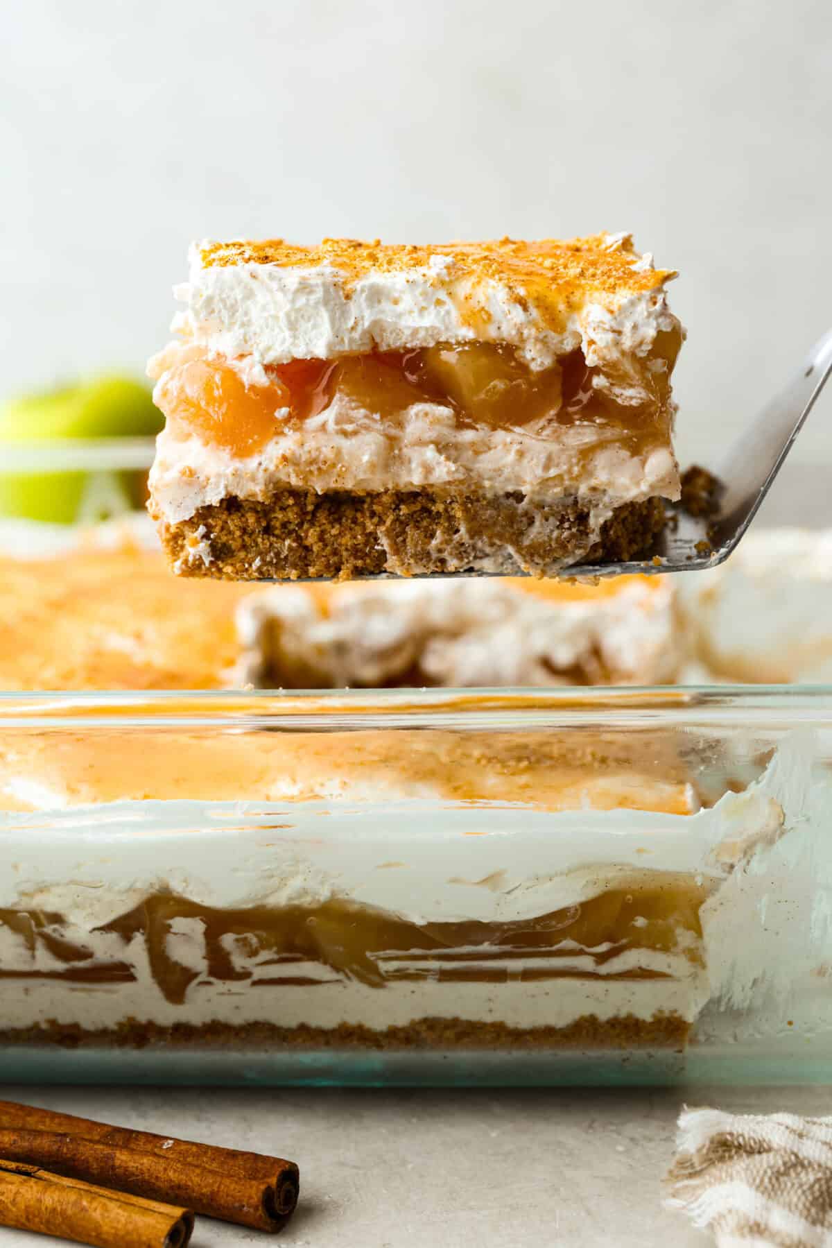 Caramel Apple Pie Lush is the easiest fall dessert you’ll ever make! With layers of buttery crust, creamy cheesecake, spiced apples, caramel, and whipped topping, it’s a yummy fall treat that is so much easier than baking a pie from scratch! Slice of caramel apple pie lush being lifted out of the pan.