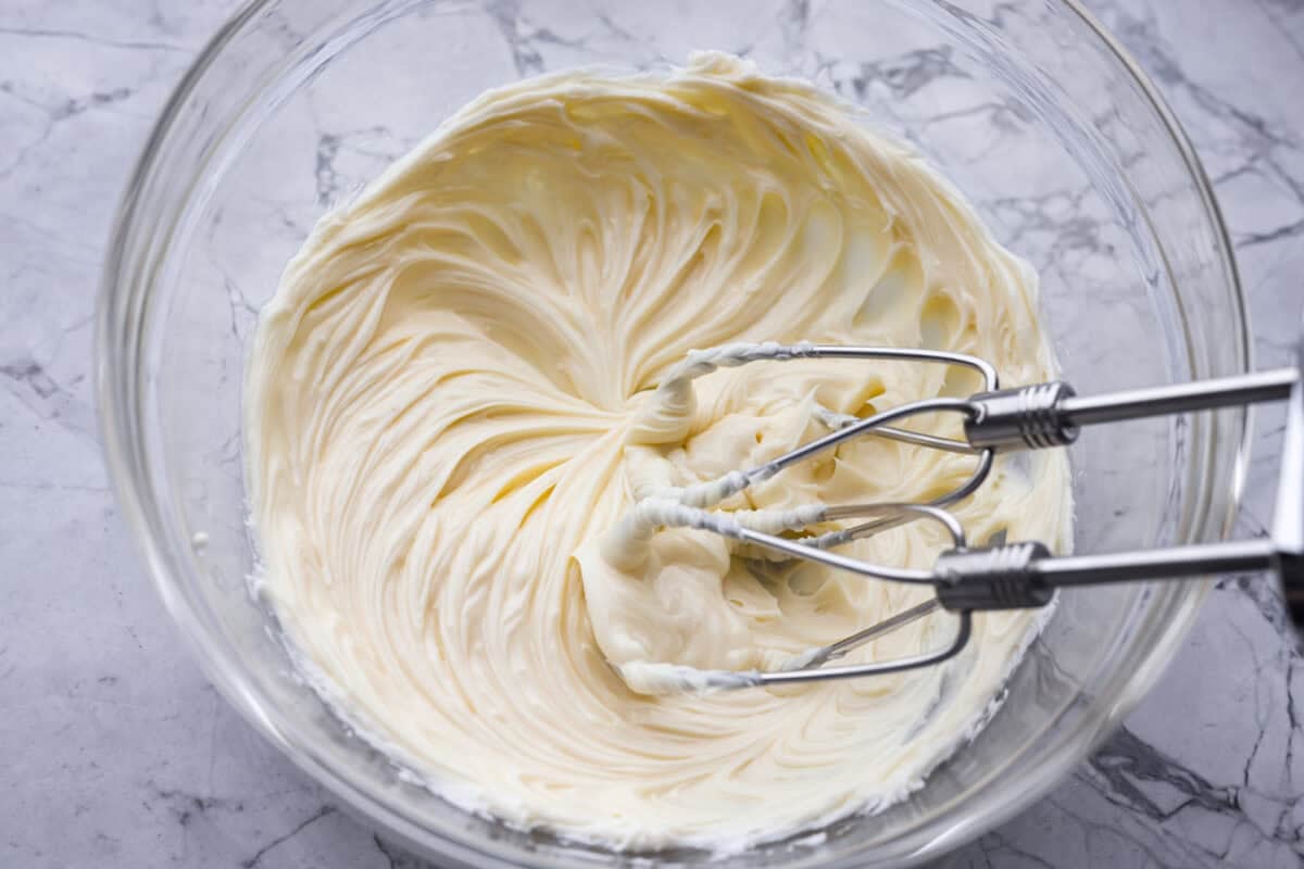 White chocolate melted and butter being mixed together with a hand mixer.