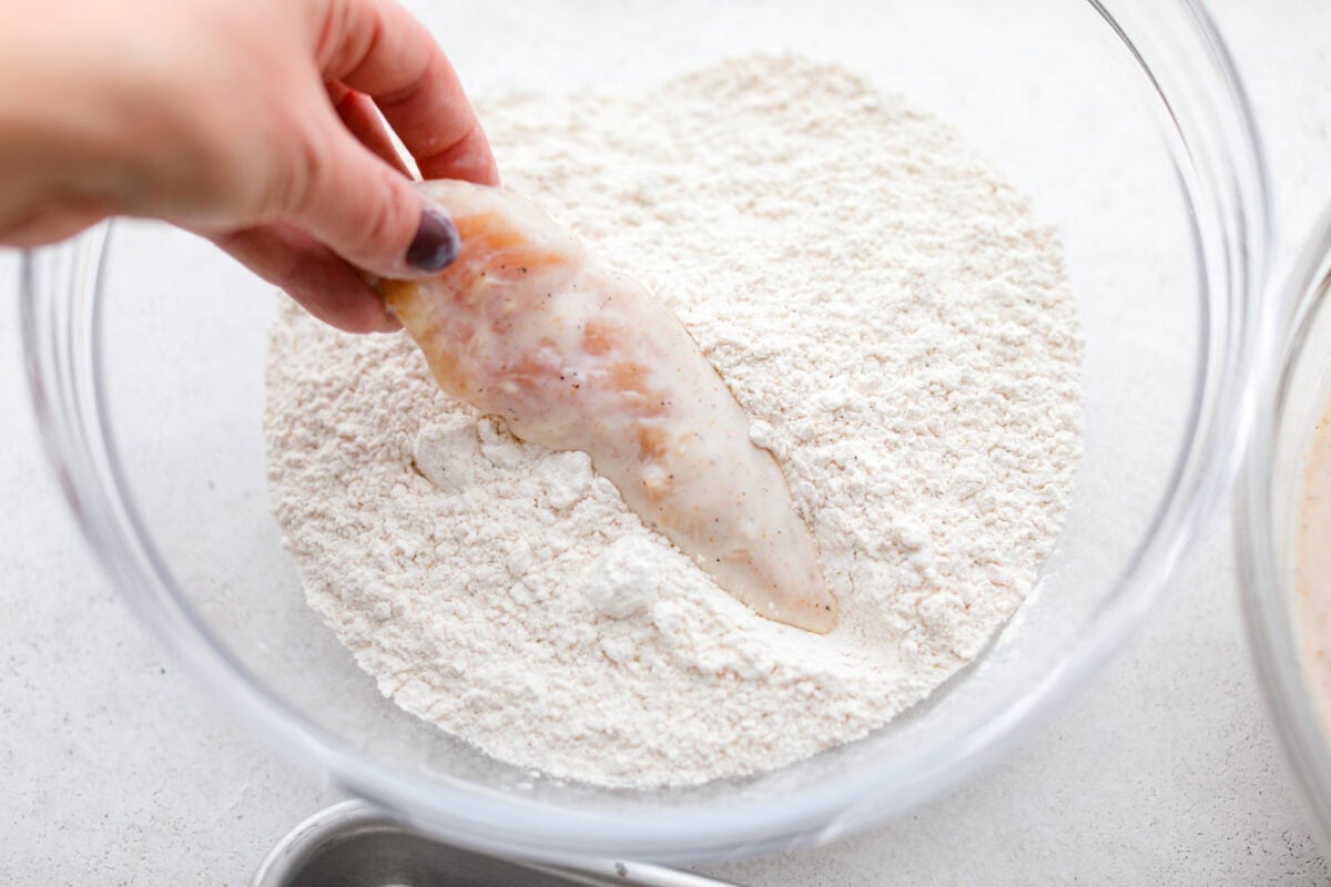 Make this copycat Raising Cane’s chicken tenders at home, no drive-thru required. An easy marinade, simple ingredients, and a quick fry give you crisp, light chicken and that unmistakable Cane’s sauce for a fraction of the cost. Someone dipping a marinated chicken tender into the bowl of breading ingredients.