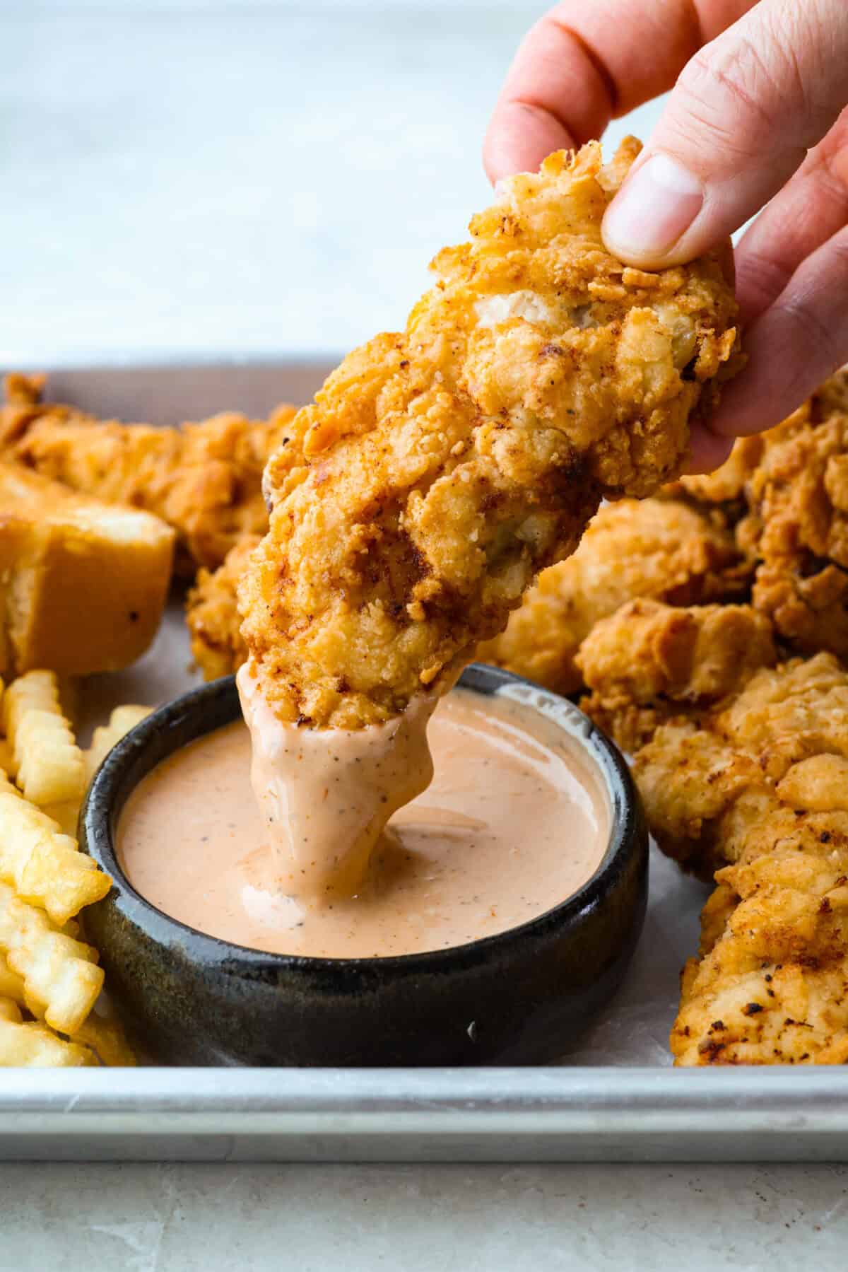 Make this copycat Raising Cane’s chicken tenders at home, no drive-thru required. An easy marinade, simple ingredients, and a quick fry give you crisp, light chicken and that unmistakable Cane’s sauce for a fraction of the cost. Someone dipping a Raising Cane's chicken into a small bowl of Cane's sauce.