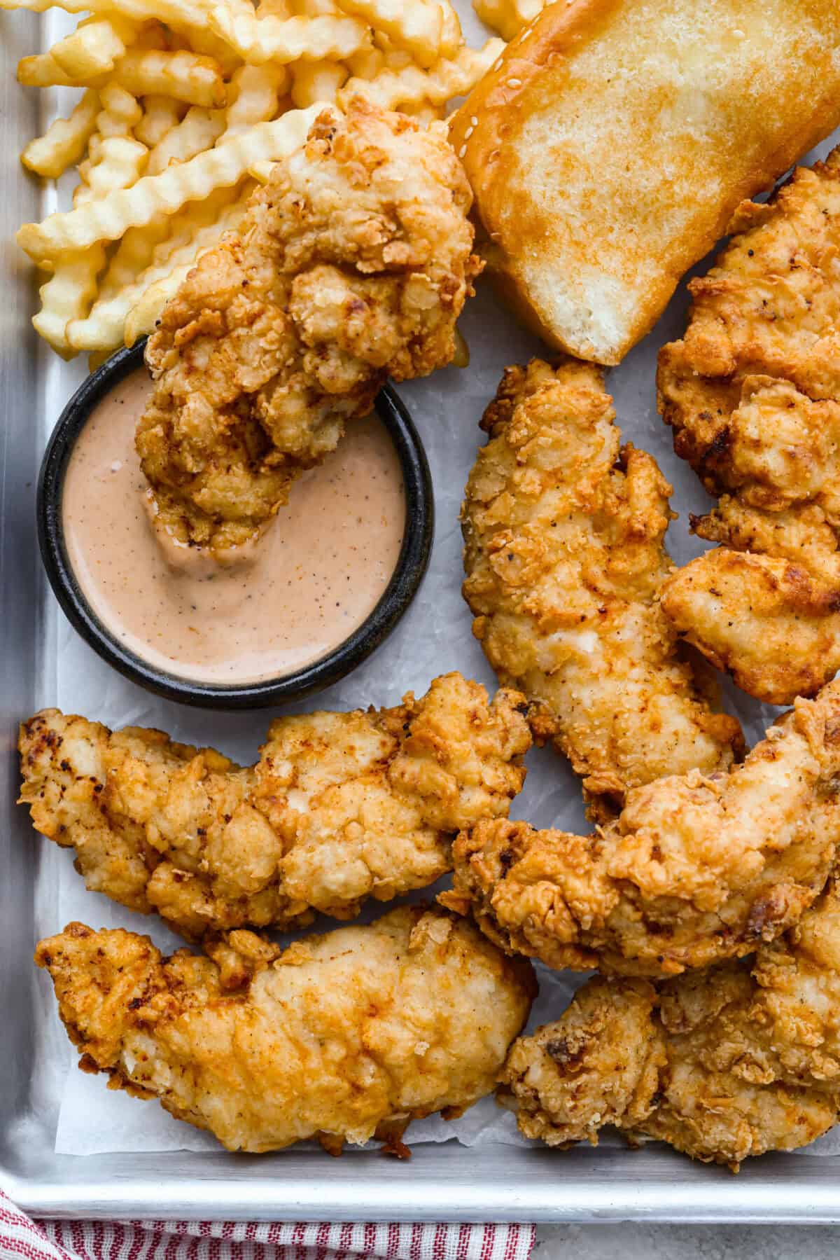 Make this copycat Raising Cane’s chicken tenders at home, no drive-thru required. An easy marinade, simple ingredients, and a quick fry give you crisp, light chicken and that unmistakable Cane’s sauce for a fraction of the cost. Crispy Raising Cane's chicken tenders on a plate next to crinkle cut fries, Texas toast, and a small bowl of Cane's dipping sauce.