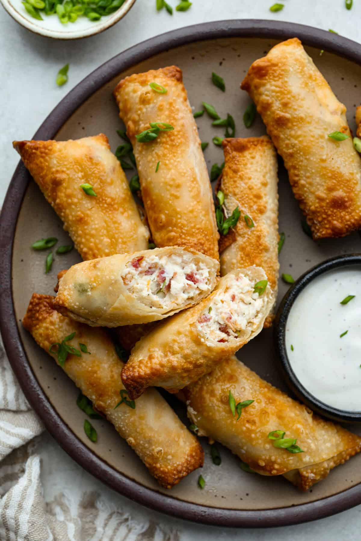 Crack Chicken Egg Rolls wrap savory chicken, crispy bacon, melty cheese, and zesty ranch in a golden, crunchy shell. Easy to make, lighter than deep-fried versions, and perfect for parties or game day! Platter of crack chicken egg rolls with a small bowl of dipping sauce.
