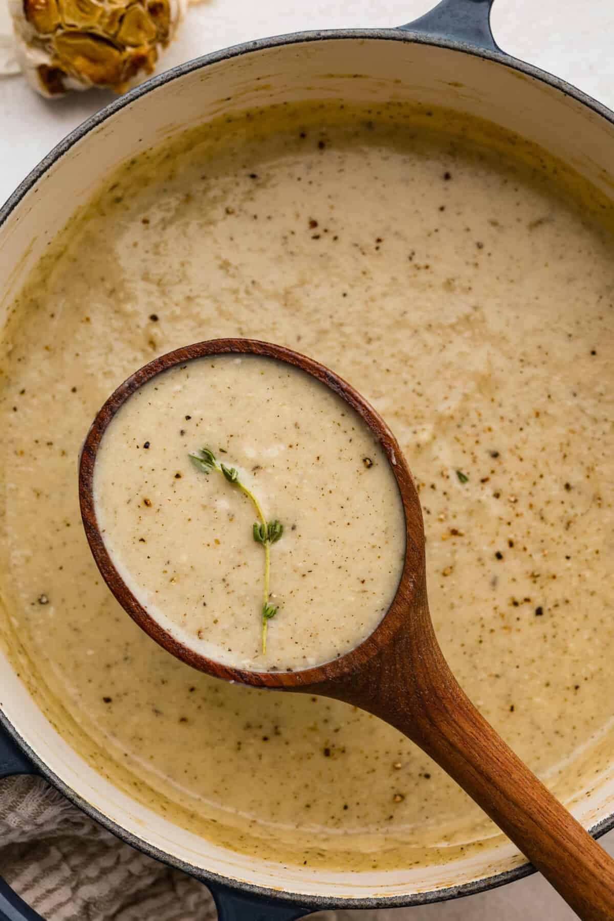 Pot of roasted garlic soup with wooden ladle. 