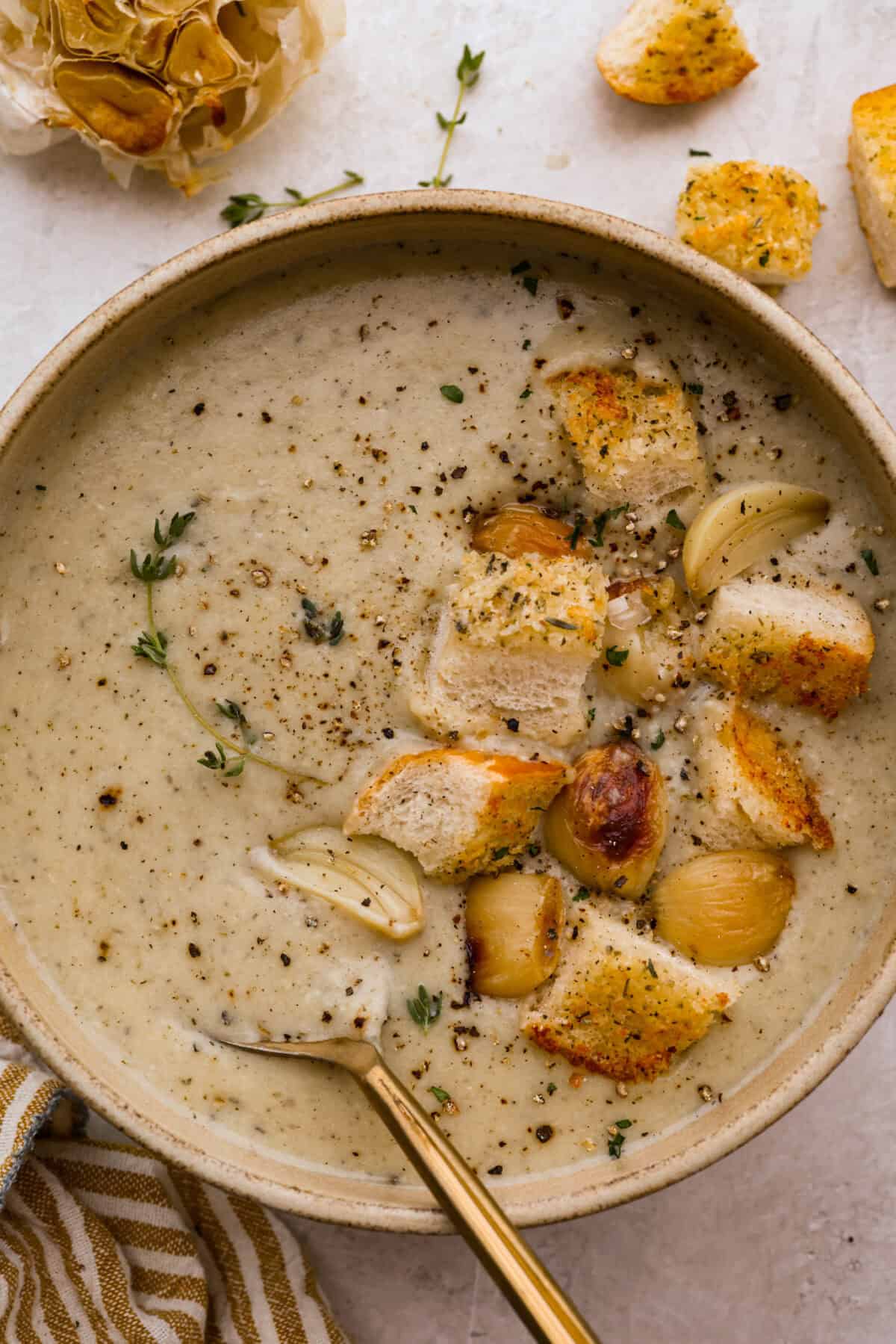 Bowl of roasted garlic soup toped with croutons, garlic cloves and pepper. 