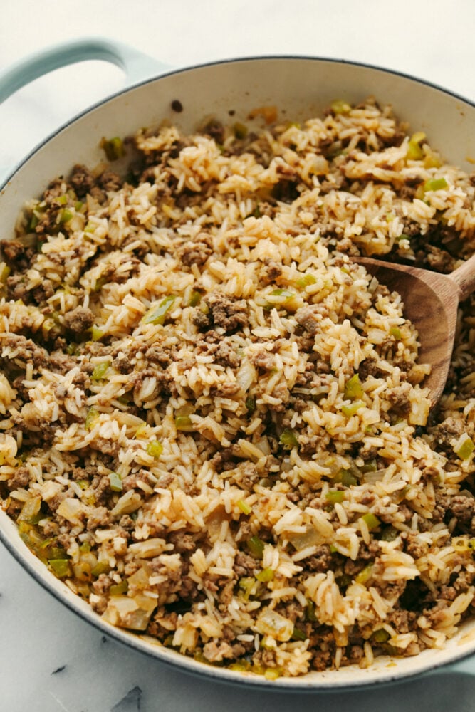 Why is it called “dirty” rice? The rice gets brown as it cooks with meat, Cajun spices, and the holy trinity of Cajun cooking: onion, bell pepper, and celery. My version combines ground pork and beef for a flavorful twist on this Louisiana classic! Dirty rice with meat and veggies being served with a wooden spoon.