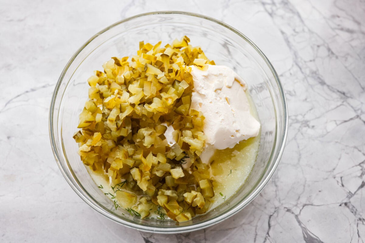 Meet my Fried Pickle Dip...a viral take on my popular pickle dip! The toasted bread crumbs elevate the flavors with the crunchy "fried" texture. Chopped pickles and other ingredients added to a bowl.