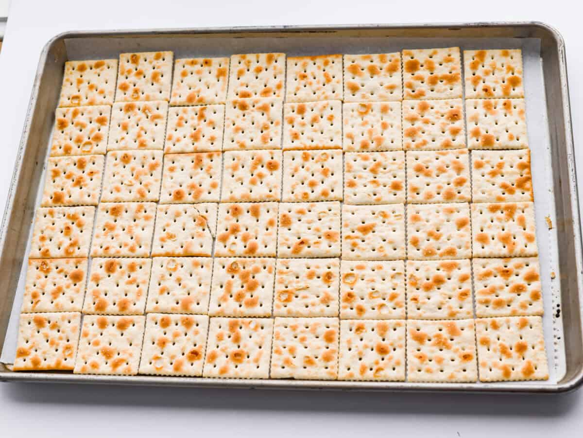 Saltine crackers spread out on a cookie sheet.
