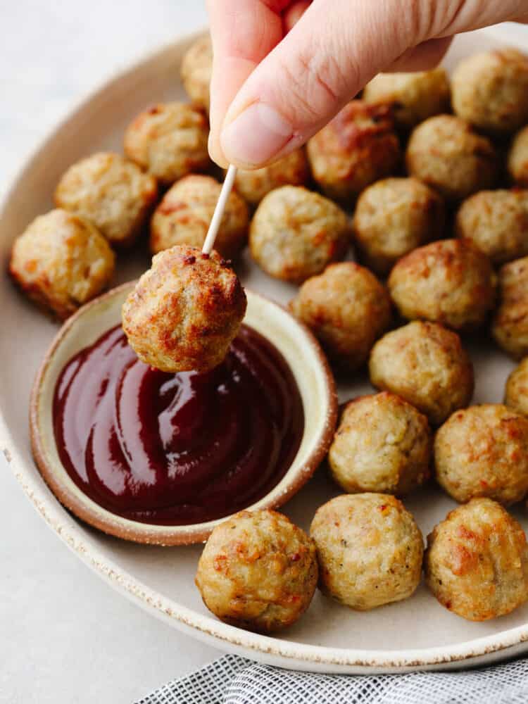 Okay, hear me out, frozen meatballs in the air fryer are a total game-changer. They come out crispy on the outside, juicy on the inside, and taste like you made them from scratch (but without the effort). I use them ALL the time! A meatballs with a toothpick being dipped into BBQ sauce.