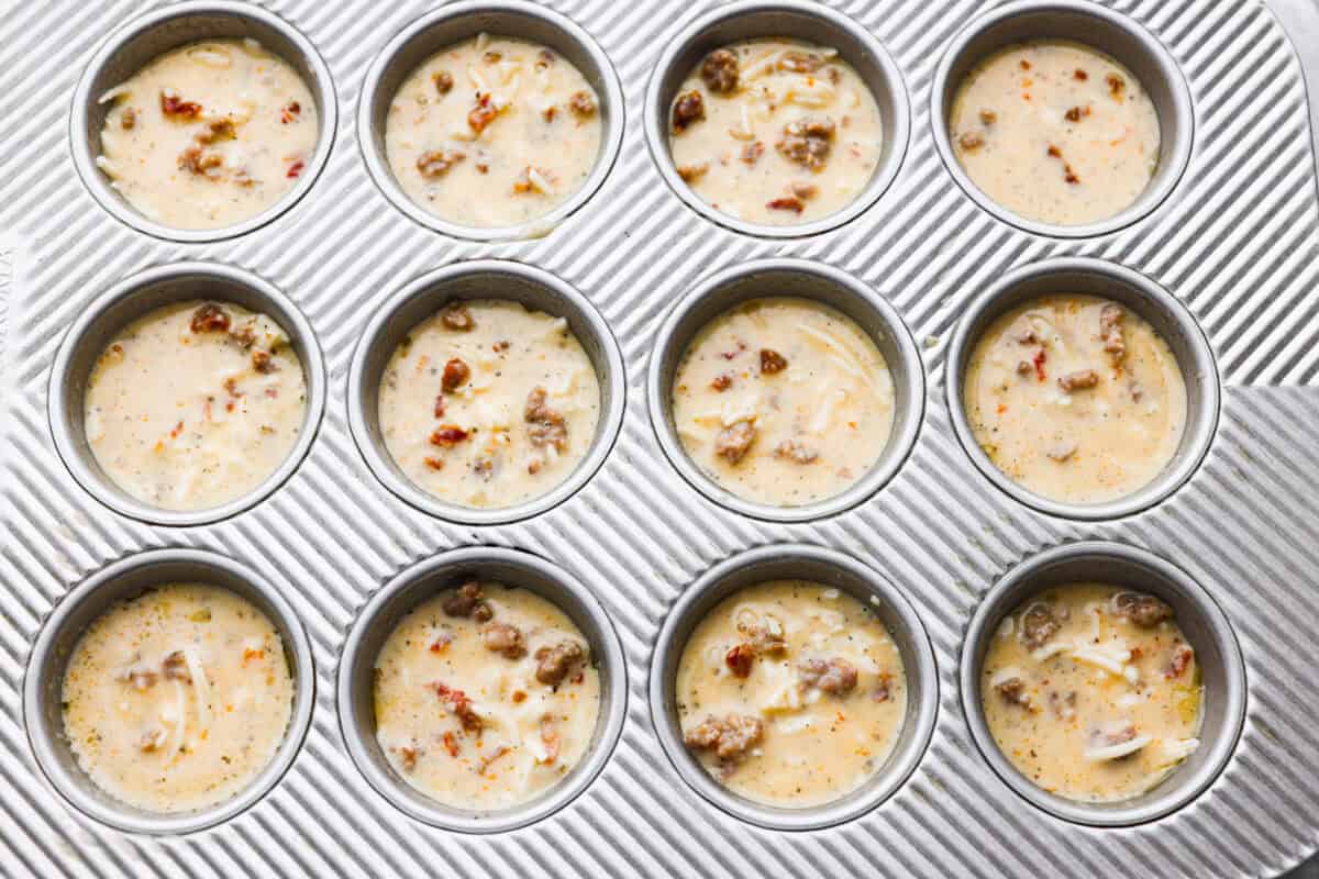 Use a measuring cup to scoop the egg mixture into the wells of the muffin tin, filling them no more than ⅔ of the way full. Try to disperse the sausage evenly throughout the muffin wells. Sausage and egg mixture added to muffin tin, ready to be baked.