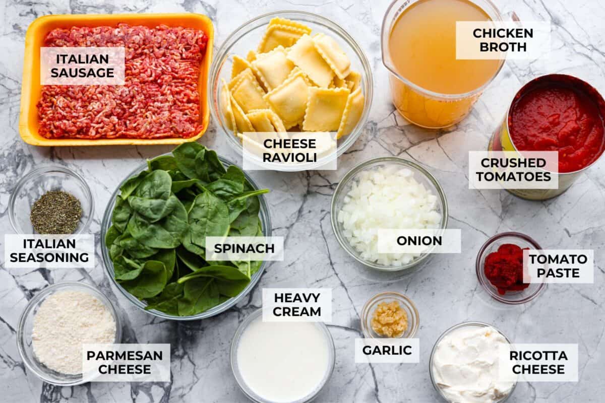 Million Dollar Soup is creamy, comforting, and worth every indulgent bite! The rich tomato soup base is loaded with sausage, cheesy ravioli, and heavy cream. The dollop of ricotta cheese on top is a MUST! Overhead shot of labeled million dollar soup ingredients.