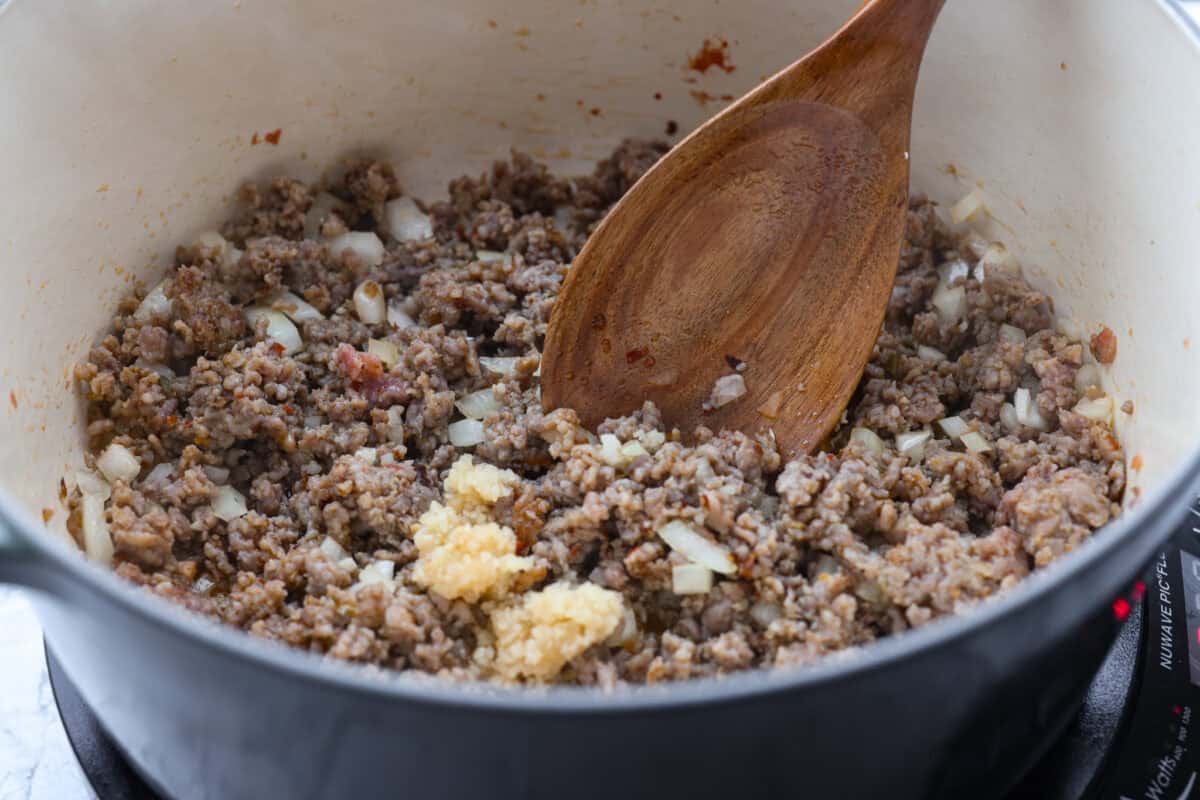 Million Dollar Soup is creamy, comforting, and worth every indulgent bite! The rich tomato soup base is loaded with sausage, cheesy ravioli, and heavy cream. The dollop of ricotta cheese on top is a MUST! Italian sausage, onion, and garlic cooking in a pot.