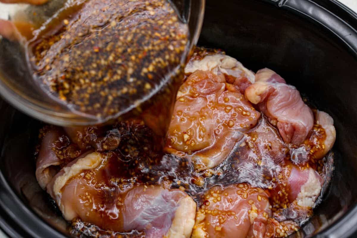 Set it and forget it! This slow cooker Korean BBQ chicken is sweet, savory, and just the right amount of spice. Perfect for tossing over rice, piling onto buns, topping a salad, or even making tacos. Weeknight dinner just got easier! Sauce being poured over the chicken in the slow cooker.
