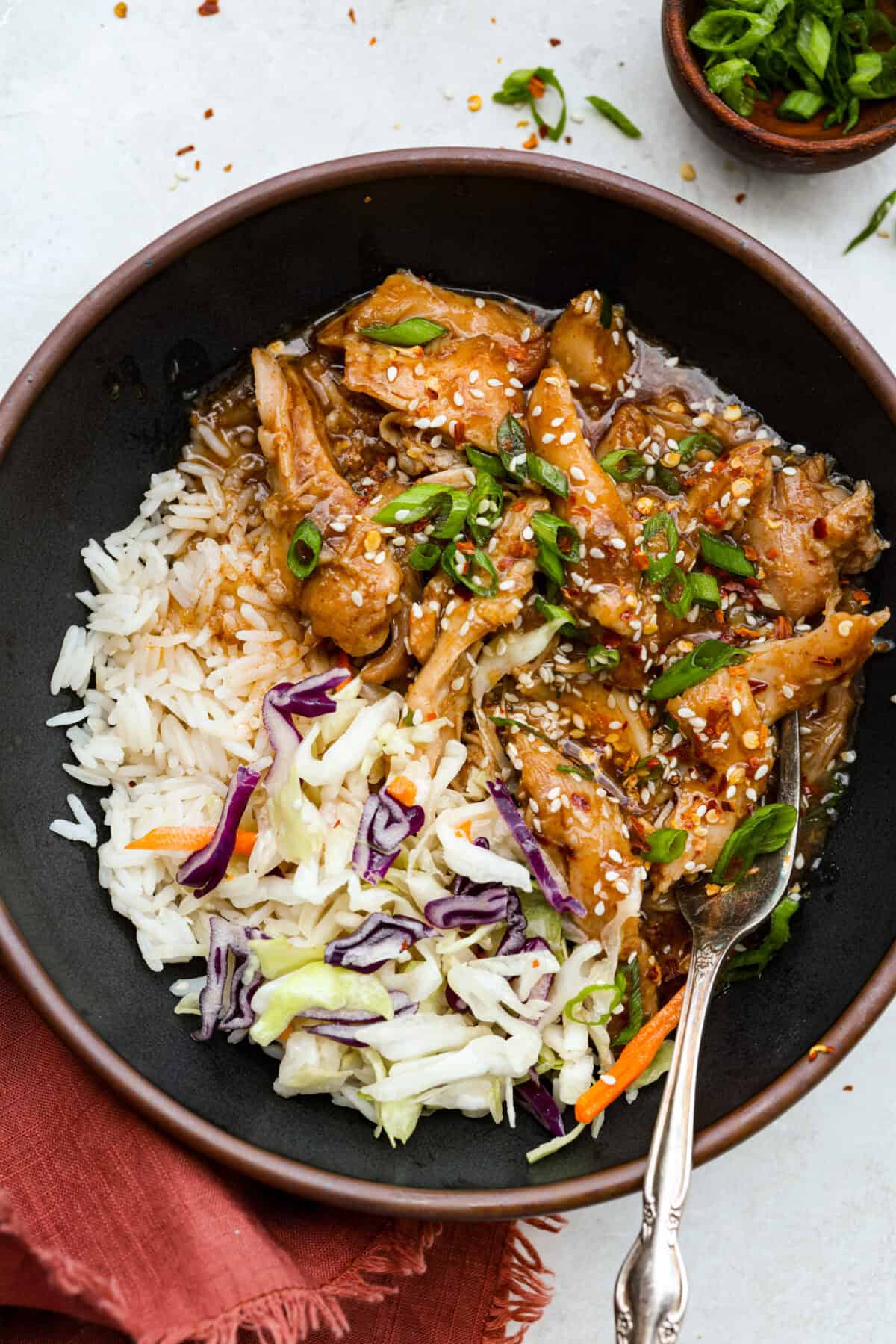 Set it and forget it! This slow cooker Korean BBQ chicken is sweet, savory, and just the right amount of spice. Perfect for tossing over rice, piling onto buns, topping a salad, or even making tacos. Weeknight dinner just got easier! Slow cooker Korean BBQ chicken in a bowl with rice and cabbage.