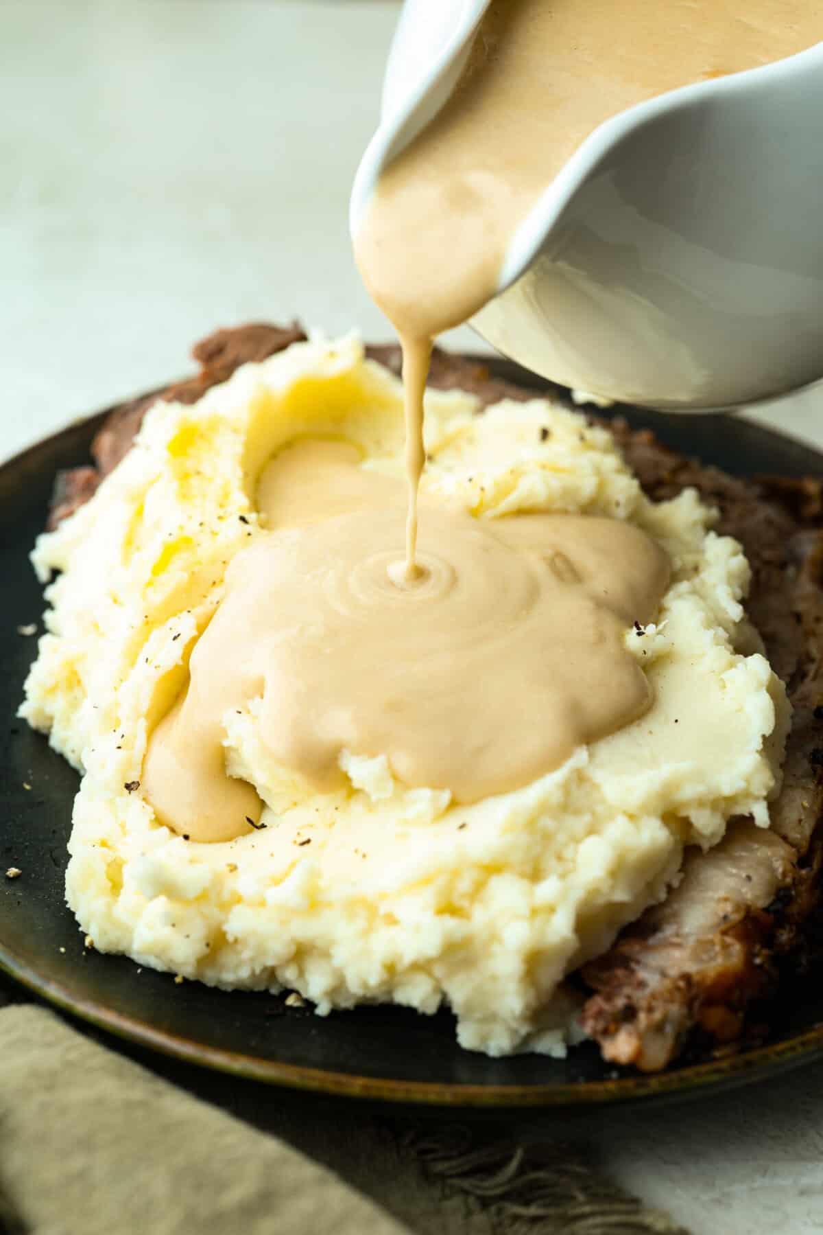 Turn those flavorful pan drippings into the creamiest gravy with a hint of tang. This sour cream gravy is rich, smooth, and so versatile. They are perfect over mashed potatoes, pork chops, but especially on my favorite Swedish Meatballs. Someone pouring sour cream gravy over mashed potatoes.