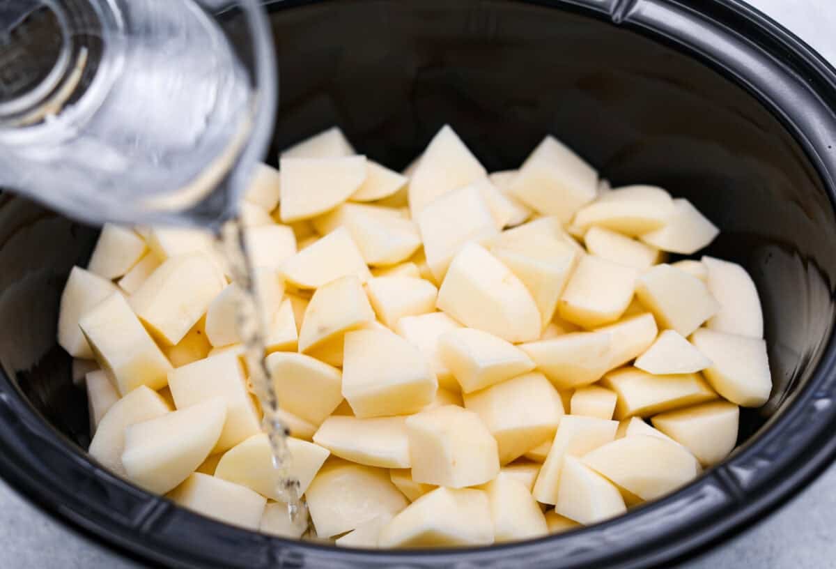 You MUST TRY these crockpot mashed potatoes! They are so creamy and delicious and super easy to make! Which makes them the perfect side for any meal. Someone pouring water in the crockpot.