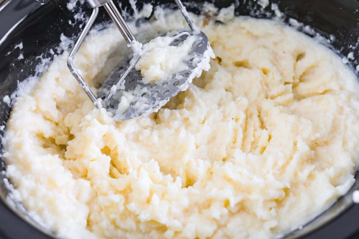 You MUST TRY these crockpot mashed potatoes! They are so creamy and delicious and super easy to make! Which makes them the perfect side for any meal. Someone mashing the potatoes in the crockpot.