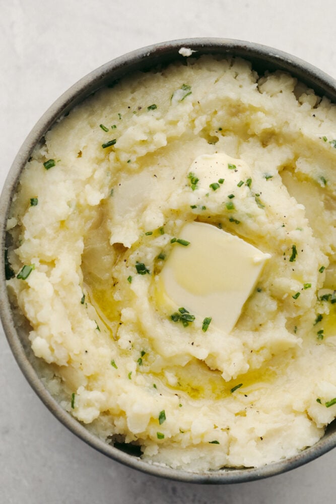 You MUST TRY these crockpot mashed potatoes! They are so creamy and delicous, plus they are super easy to make! Which makes them the perfect side for any meal. Mashed potatoes in a bowl with some butter and herbs on top.
