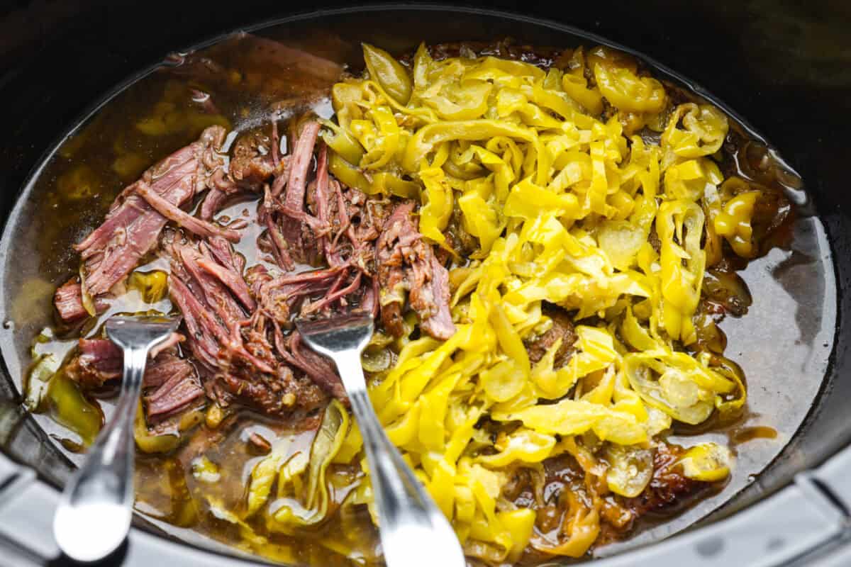 My Slow Cooker Italian Beef is tender, juicy, and loaded with zesty Italian flavor. The secret's in the way you sear the beef! This creates melt-in-your-mouth meat perfect for sandwiches or hearty dinners. Forks sticking out of the meat in the crockpot mid shred.