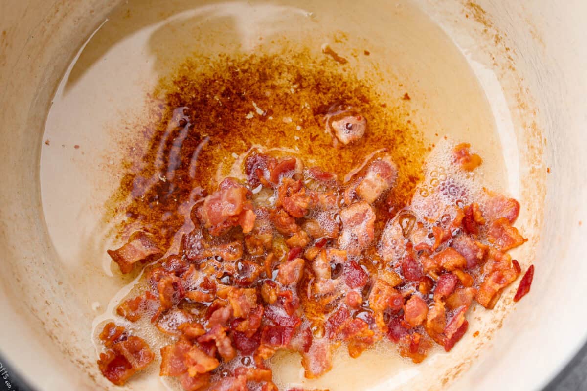 My Texas Cowboy Stew actually fills up my always-hungry boys! That's because it's loaded with smoky bacon, spicy sausage, ground beef, and potatoes. They all simmer together in a rich broth for a hearty stew. Bacon cooking in the bottom of the dutch oven.