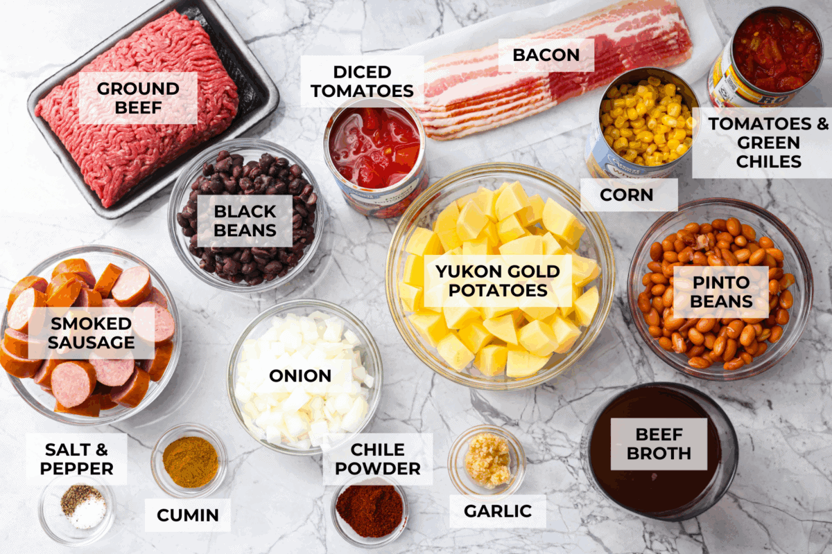 My Texas Cowboy Stew actually fills up my always-hungry boys! That's because it's loaded with smoky bacon, spicy sausage, ground beef, and potatoes. They all simmer together in a rich broth for a hearty stew. Overhead shot of labeled Texas cowboy stew ingredients.