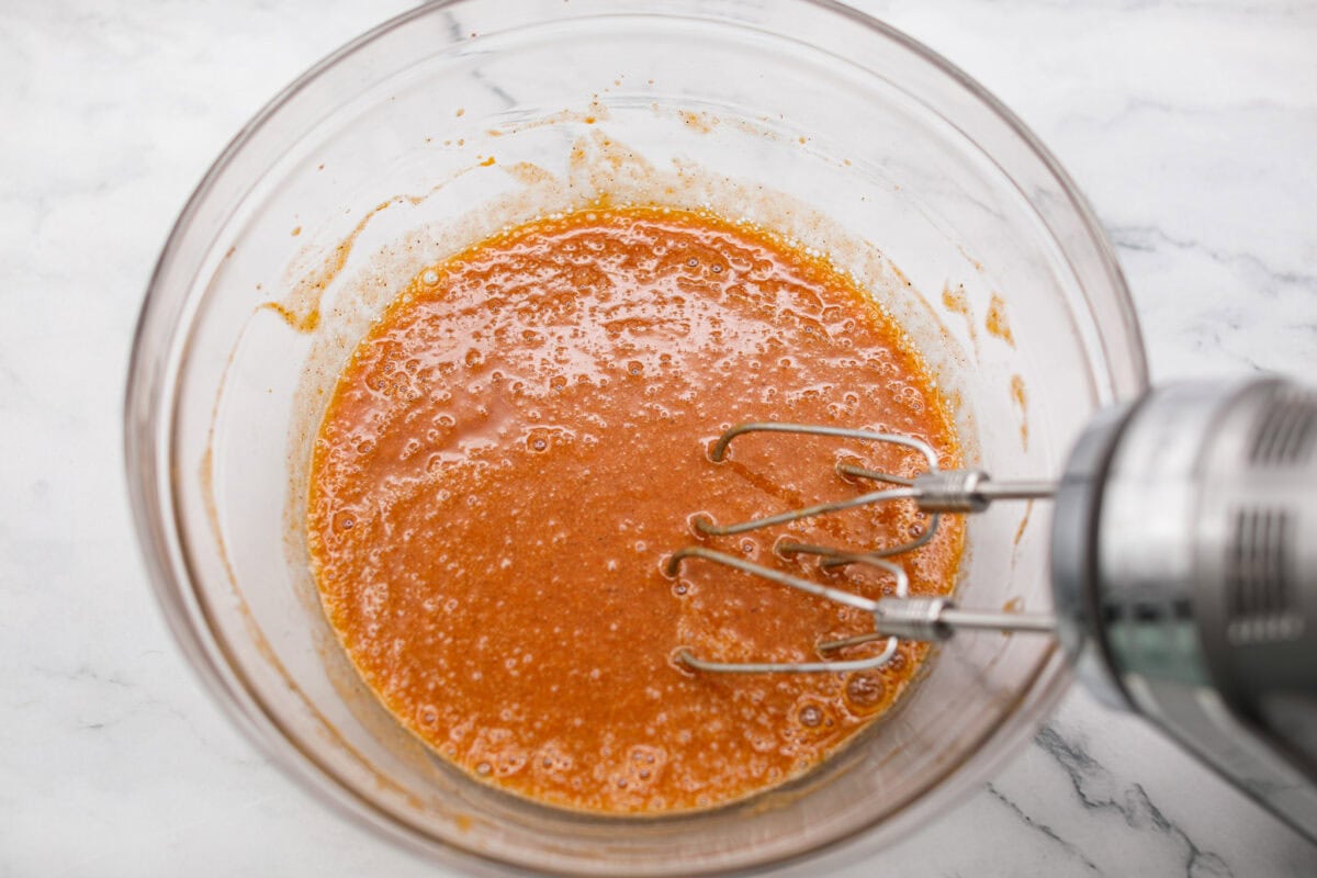 This really is the world’s best pumpkin roll! Soft, moist pumpkin cake wrapped around a sweet cream cheese filling and finished with a dusting of powdered sugar, it’s pure fall magic. The best part? It’s surprisingly easy to make. Someone using a hand mixer to beat together eggs, sugar, pumpkin, vanilla, cinnamon, and cloves.