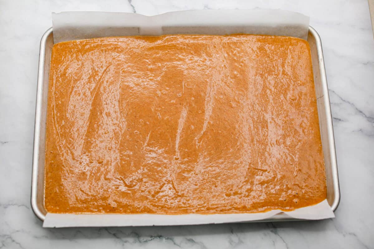 This really is the world’s best pumpkin roll! Soft, moist pumpkin cake wrapped around a sweet cream cheese filling and finished with a dusting of powdered sugar, it’s pure fall magic. The best part? It’s surprisingly easy to make. Cake batter spread out on the parchment paper on a jelly roll pan.