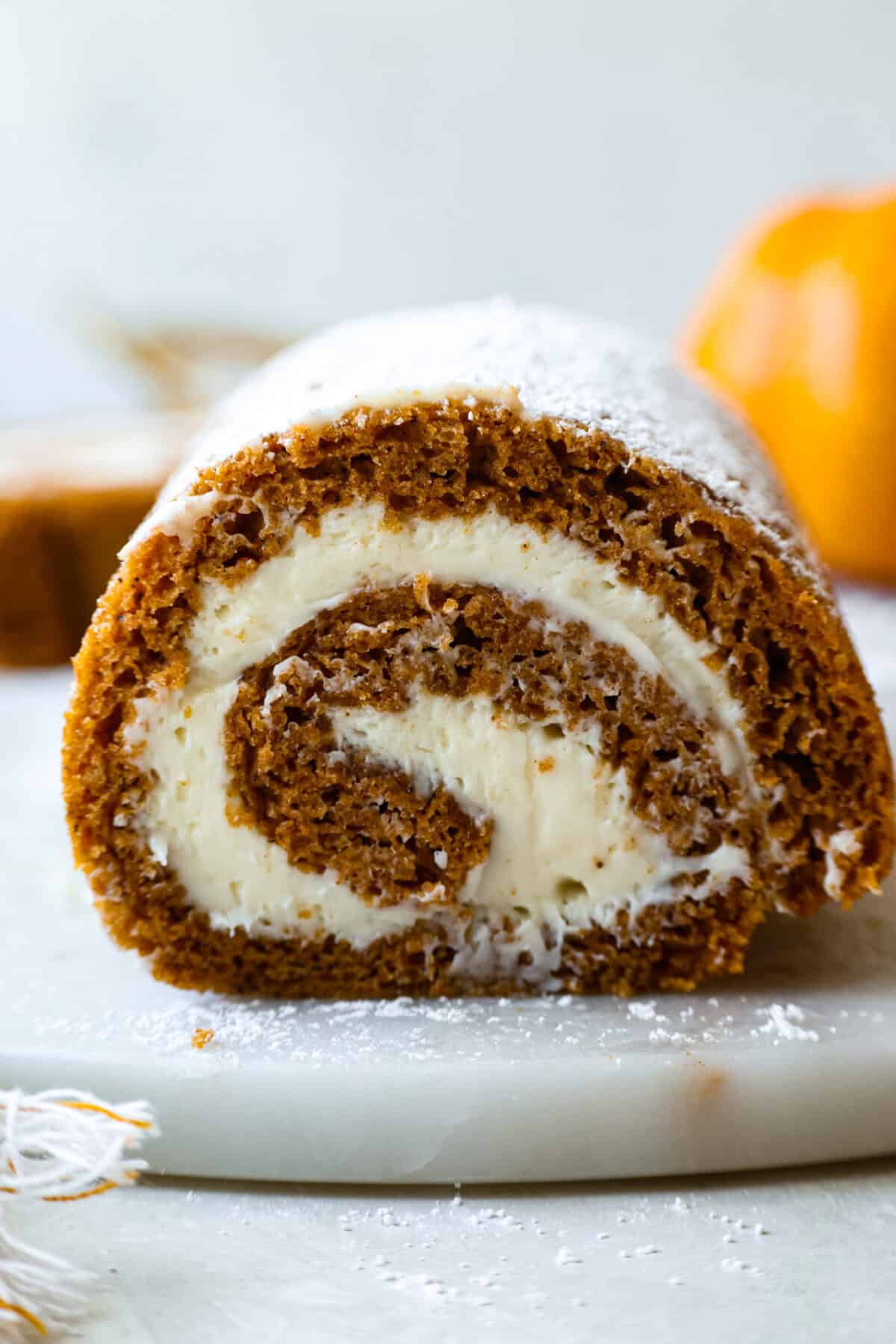 This really is the world’s best pumpkin roll! Soft, moist pumpkin cake wrapped around a sweet cream cheese filling and finished with a dusting of powdered sugar, it’s pure fall magic. The best part? It’s surprisingly easy to make. Side view of sliced pumpkin roll cake.