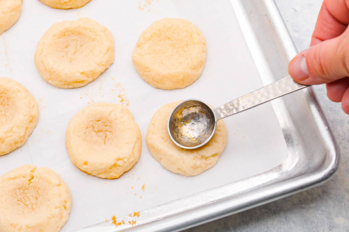 Meet the upgraded Twix thumbprint cookies! I re‑tested and updated the recipe so you'll get defined wells, clean edges, and a tender center every time! They are perfect for gift giving and cookie parties! Someone pressing the teaspoon into the baked cookies.