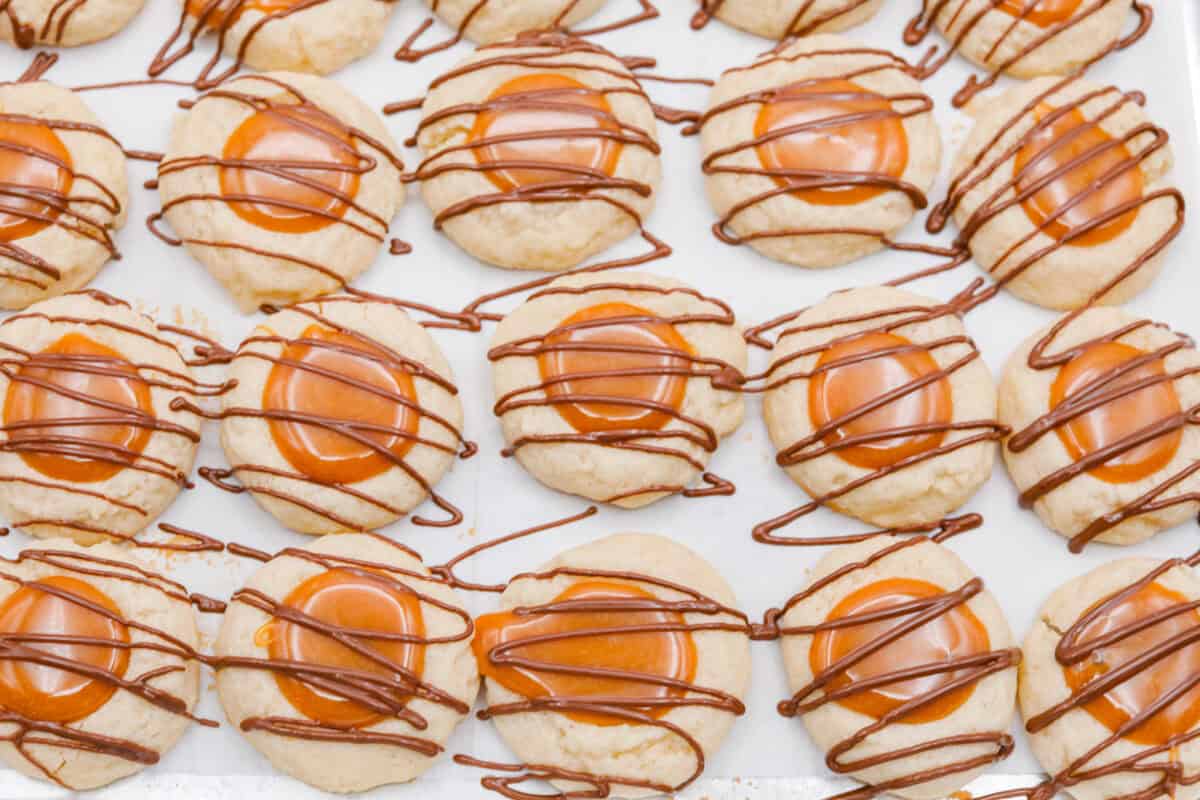 Meet the upgraded Twix thumbprint cookies! I re‑tested and updated the recipe so you'll get defined wells, clean edges, and a tender center every time! They are perfect for gift giving and cookie parties! Chocolate drizzled over the top of the Twix thumbprint cookies.