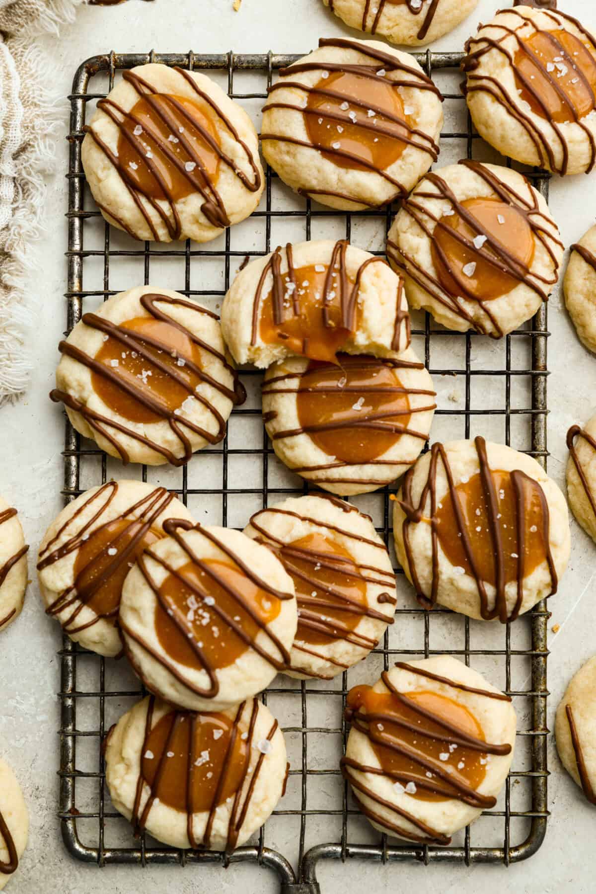 Meet the upgraded Twix thumbprint cookies! I re‑tested and updated the recipe so you'll get defined wells, clean edges, and a tender center every time! They are perfect for gift giving and cookie parties! Overhead shot of Twix thumbprint cookies on a cooling rack.