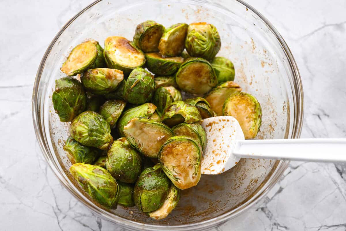 Someone stirring the Brussels sprouts with the brown sugar sauce. 