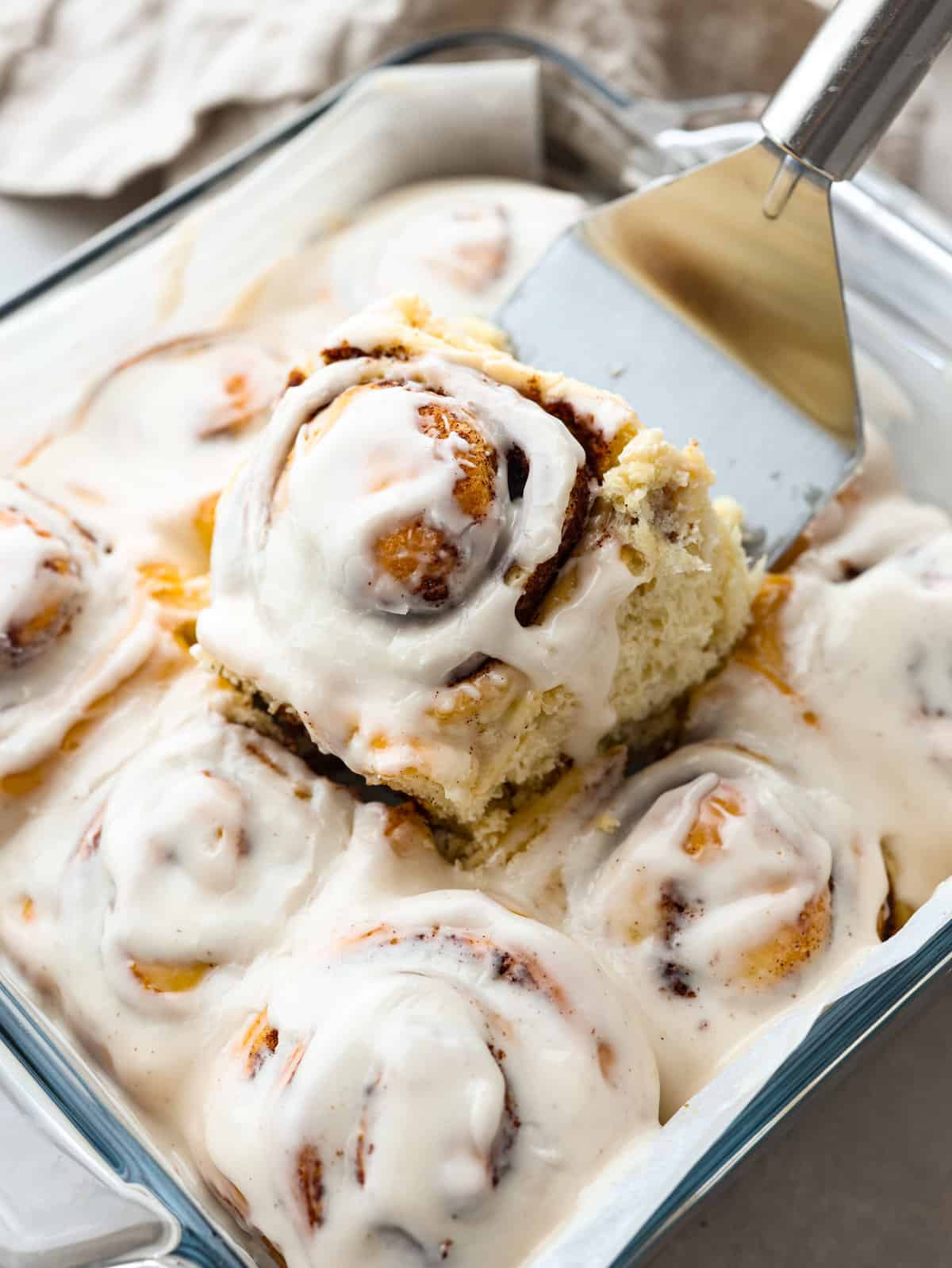 Consider this your cinnamon roll home base. Recipes are organized by skill level, from quick beginner rolls to overnight bakery-style ones, plus fun variations the whole family will love. You will also find helpful tips for dough, rising, shaping, and frosting, so every batch turns out amazing. Someone lifting a cinnamon roll our of a baking dish.