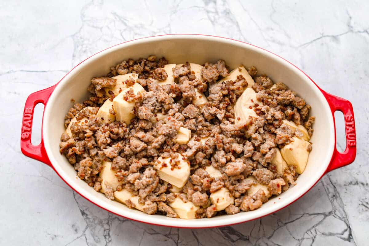 Wake up to a breakfast that feels like a warm hug! This Christmas morning casserole turns sausage, eggs, cheese, and fluffy biscuits into the easiest, hearty breakfast you can't get enough of! Cooked sausage and cut up biscuits together in a baking dish.