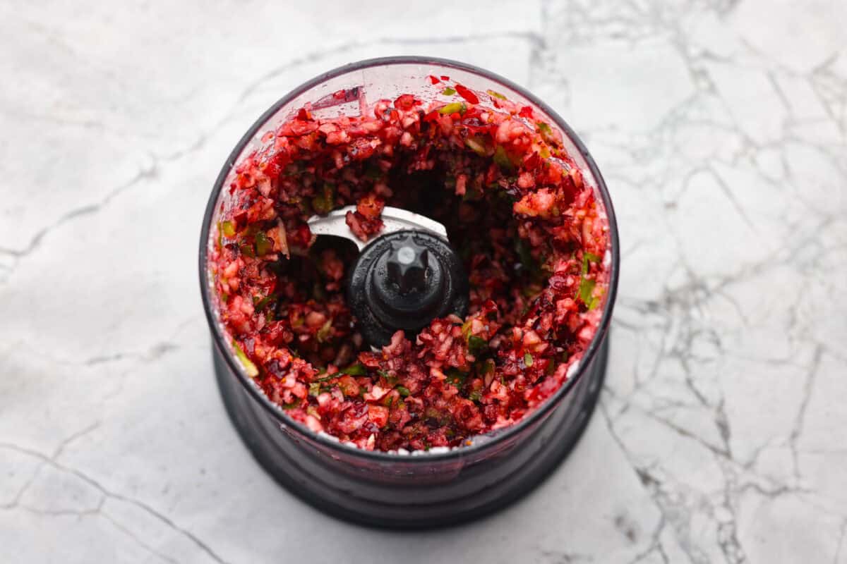 This cranberry jalapeño dip is my fresh take on the cult favorite Costco version. It's bright, tangy, a little spicy, and wildly easy to make at home. It’s the same addictive flavor, but you get to make it how you like! Cranberries, onions, jalapeños, sugar, and lime juice in a food processor.
