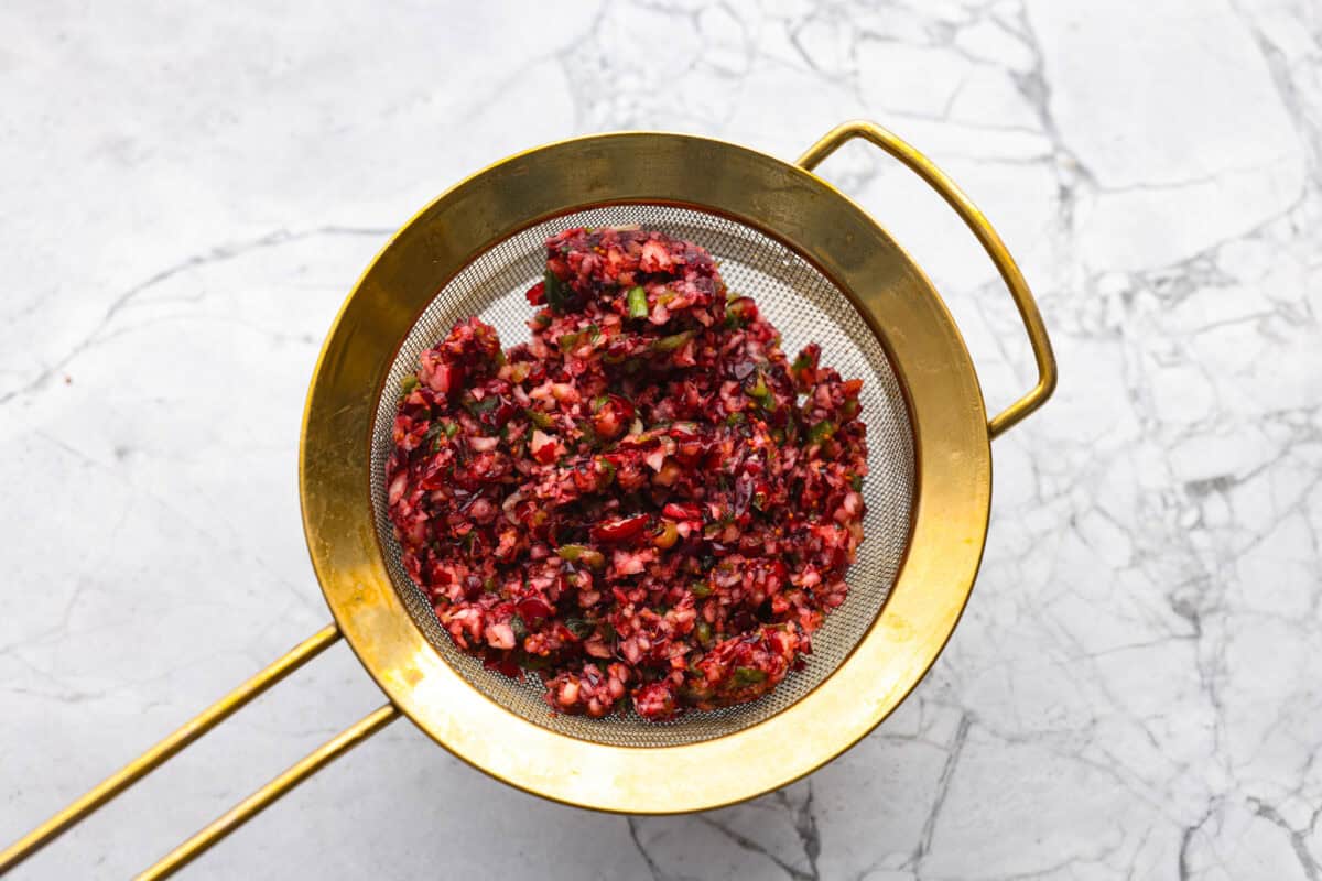 This cranberry jalapeño dip is my fresh take on the cult favorite Costco version. It's bright, tangy, a little spicy, and wildly easy to make at home. It’s the same addictive flavor, but you get to make it how you like! Cranberry mixture in a fine mesh strainer being drained.