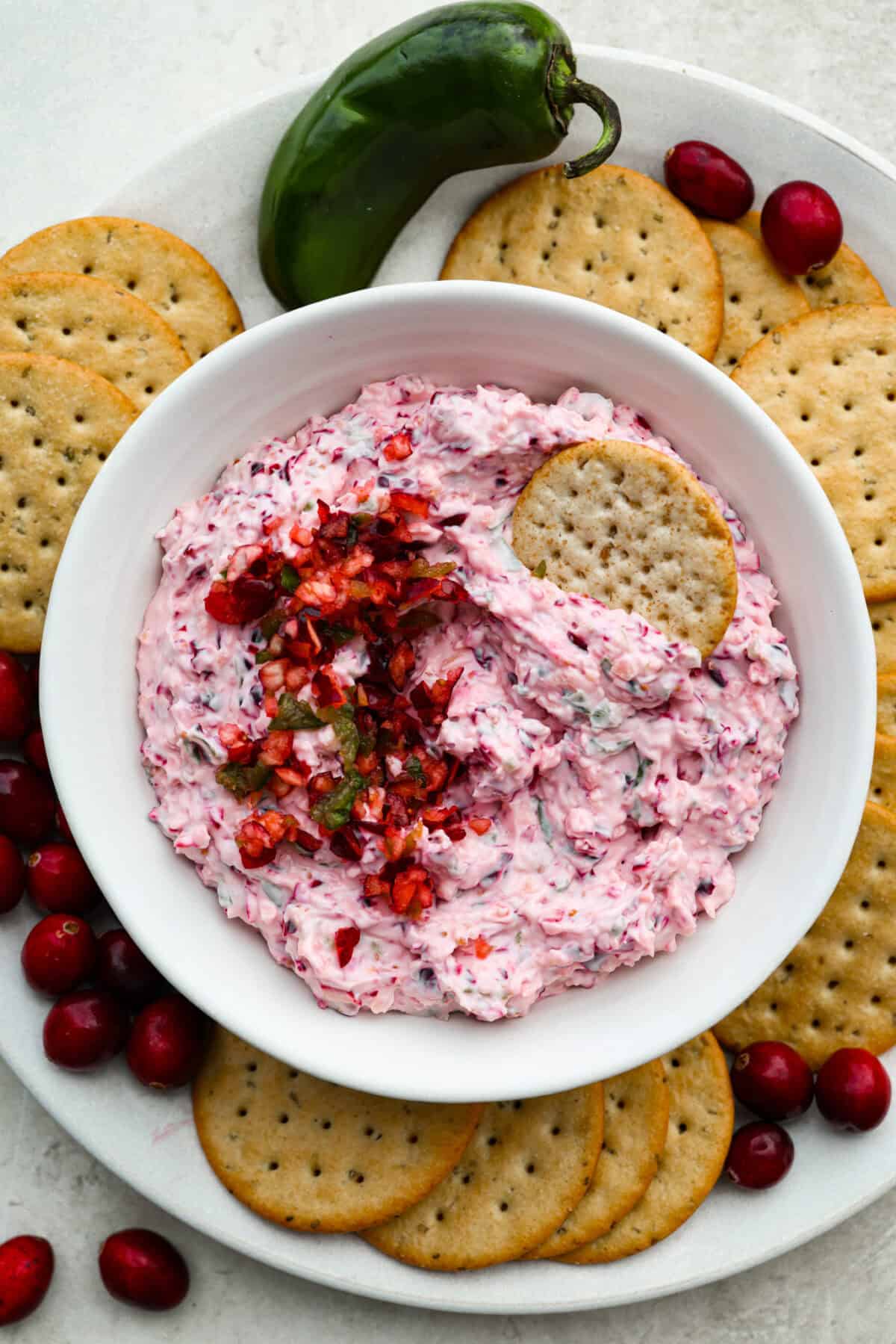 This cranberry jalapeño dip is my fresh take on the cult favorite Costco version. It's bright, tangy, a little spicy, and wildly easy to make at home. It’s the same addictive flavor, but you get to make it how you like! Bowl of cranberry jalapeño dip surrounded by crackers, cranberries and jalapeños.