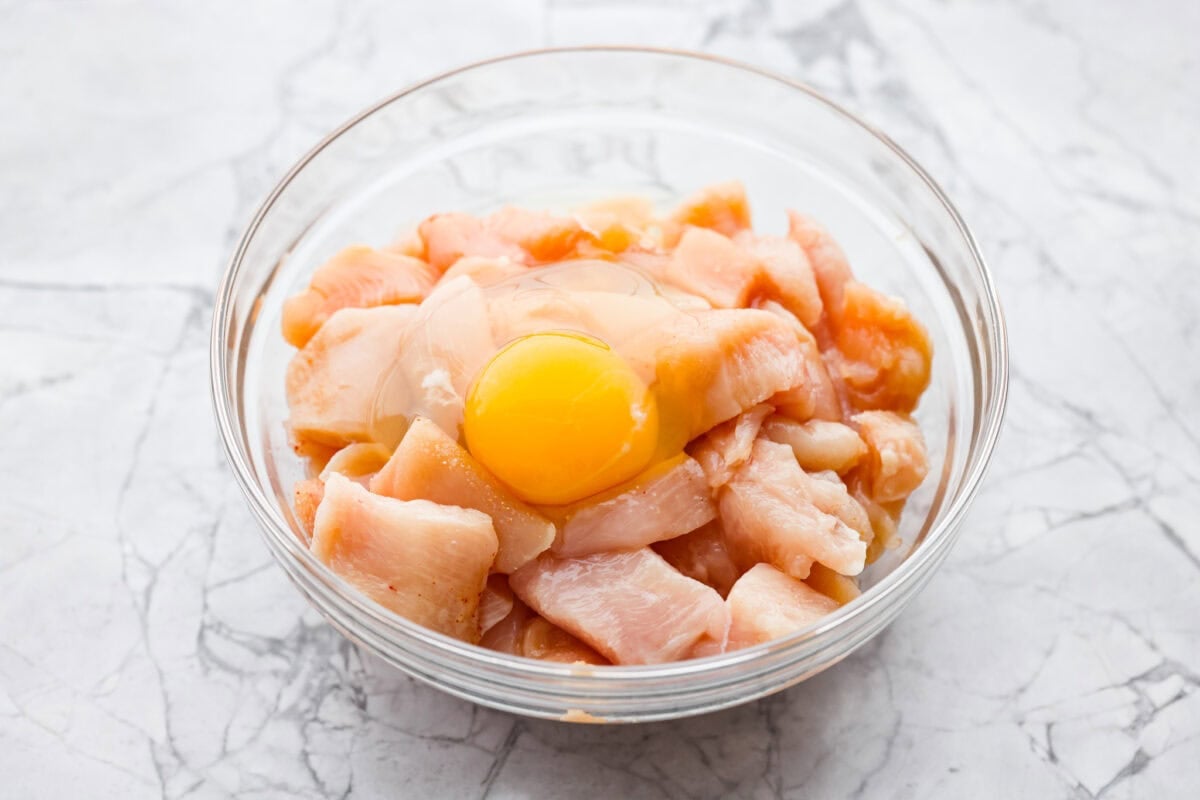 Crispy, saucy, and packed with flavor, this sweet chili chicken is a weeknight winner! Tender chicken bites get a crunchy coating, then get tossed in a sticky, sweet, and slightly spicy sauce that’s impossible to resist. Bowl of seasoned chicken with a cracked egg on top.